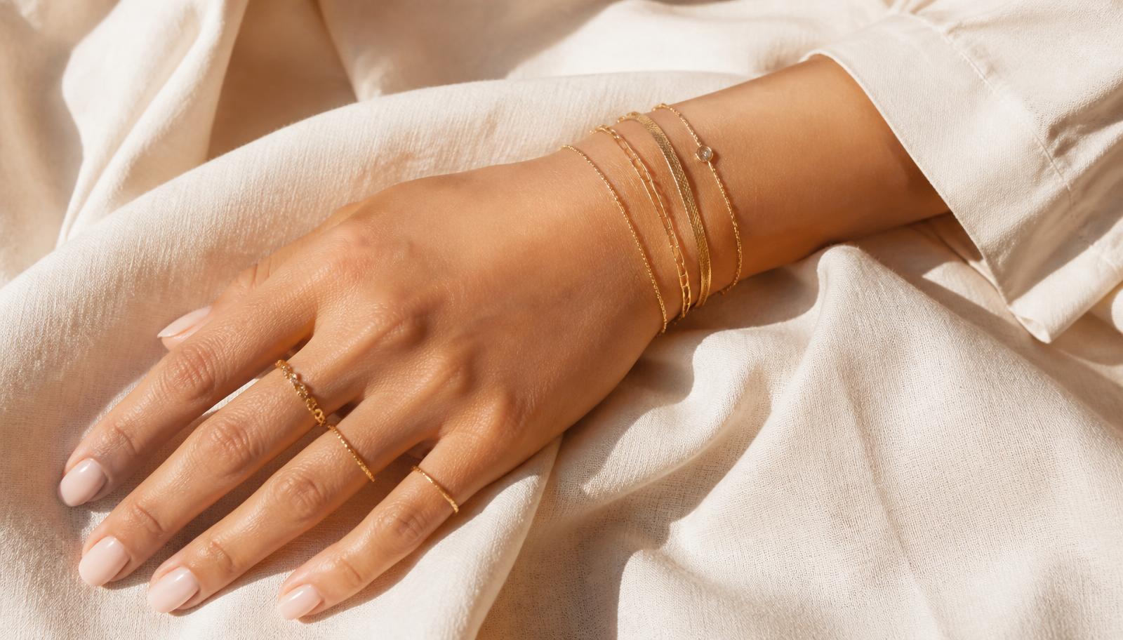 Stacked fine gold bracelets and rings on cream linen
